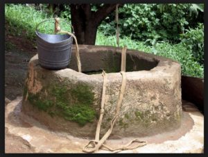 Photo of a hand dug potable water well with a bucket and rope for extraction